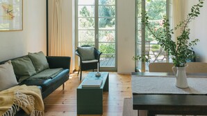 A living room with a sofa, a coffee table, a chair, and a dining table with a vase. - Tower villa apartment with pergola at Mühlenberg (Werder (Havel))