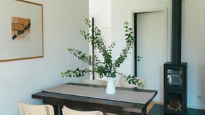 A dining area with a table, two chairs, a vase with a plant, a framed picture on the wall, and a wood-burning stove. - Tower villa apartment with pergola at Mühlenberg (Werder (Havel))
