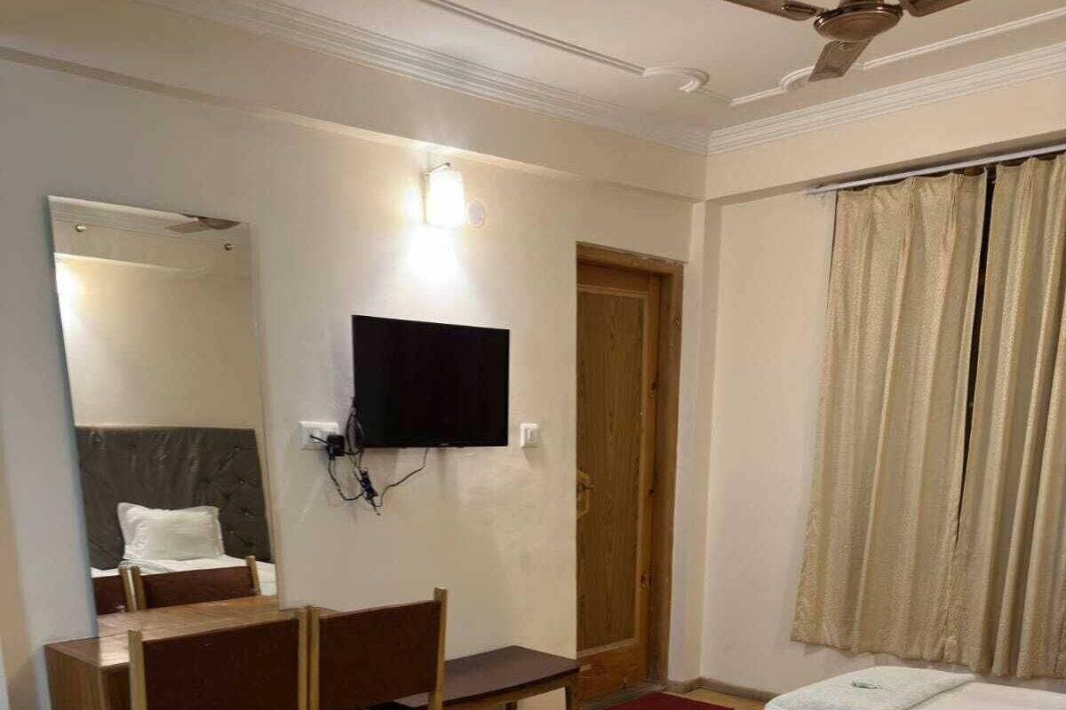 A bedroom with a bed, a desk, a chair, a television, and a ceiling fan.