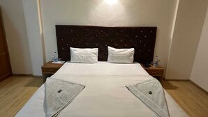 A hotel room with a bed, a nightstand, a wall-mounted light, and a ceiling fan. - Hotel Dimbir Regency (Leh)