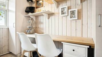 A wooden desk with two white chairs, a shelf with decorative items, and framed pictures on the wall.