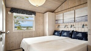 A bedroom with a large bed, a window with a view, wooden walls, and a ceiling light.