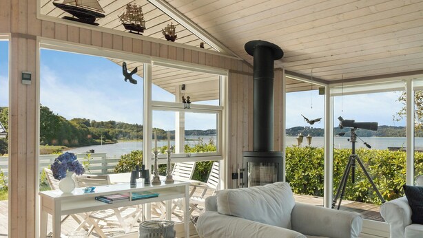 A spacious room with a large window overlooking a lake, a white table with chairs, and a white sofa.