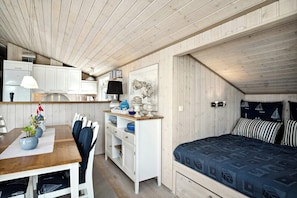 Een knus kamertje met een houten plafond, een bed met beddengoed met een patroon, een bureau met een stoel en een kitchenette.