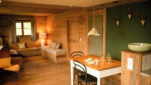 Ett mysigt rum inrett som en stuga, med trägolv, ett matbord med stolar, en soffa och en grön accentvägg med upphängda djurskallar.