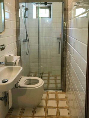 Et badeværelse med glasbrusekabine, toilet og håndvask.