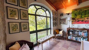 Um quarto acolhedor com uma ampla janela em arco, um banco estofado, uma estante de madeira e obras de arte emolduradas nas paredes.