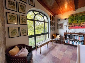 Ein gemütliches Zimmer mit einem großen Bogenfenster, einer gepolsterten Bank, einem Holzbücherregal und gerahmten Kunstwerken an den Wänden.