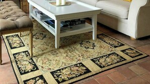 Uma sala de estar com um sofá branco, uma mesa de centro, um tapete estampado e quadros nas paredes.