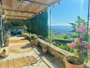 Eine Terrasse mit Blumentöpfen, einer Steinmauer und Blick ins Tal.