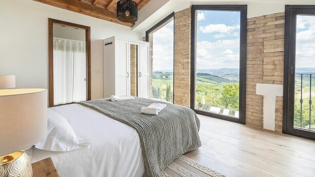 Ein Schlafzimmer mit einem Bett, einem Fenster und Blick ins Grüne.