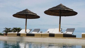 Ein Poolbereich mit Liegestühlen und Reedschirm.