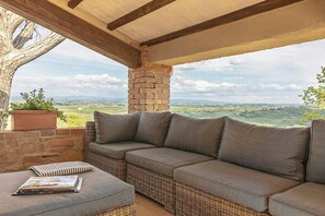 A covered outdoor seating area with a wicker sofa and a potted plant. - Restored barn in San Gimignano hills view (Pancole)