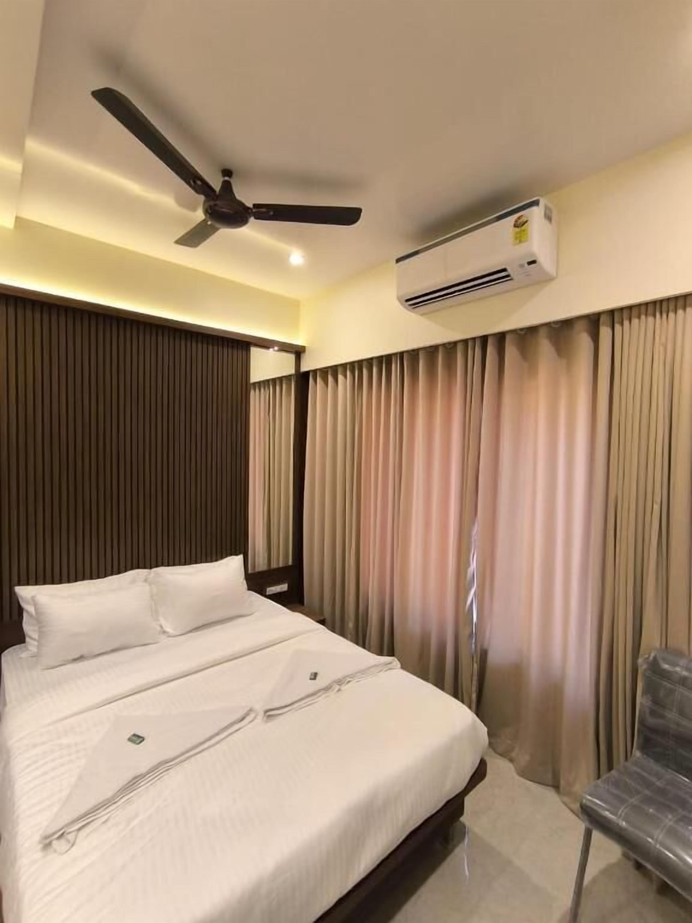 A hotel room with a bed, a ceiling fan, an air conditioning unit, and a chair.
