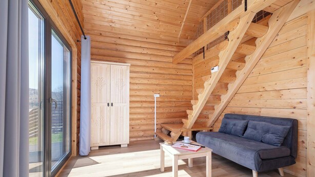 A wooden cabin interior with a sofa, table, and a staircase. - A Charming House with a Garden | Mountain View (Mutne)