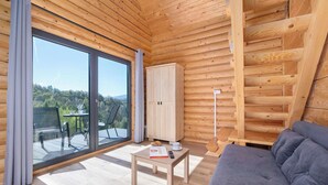 A wooden cabin interior with a sofa, a table with a book and remote, a cabinet, and a sliding glass door to a deck. - A Charming House with a Garden | Mountain View (Mutne)