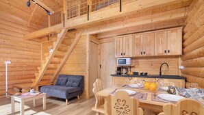A wooden cabin interior with a dining area, a sofa, a staircase, and a kitchen. - A Charming House with a Garden | Mountain View (Mutne)