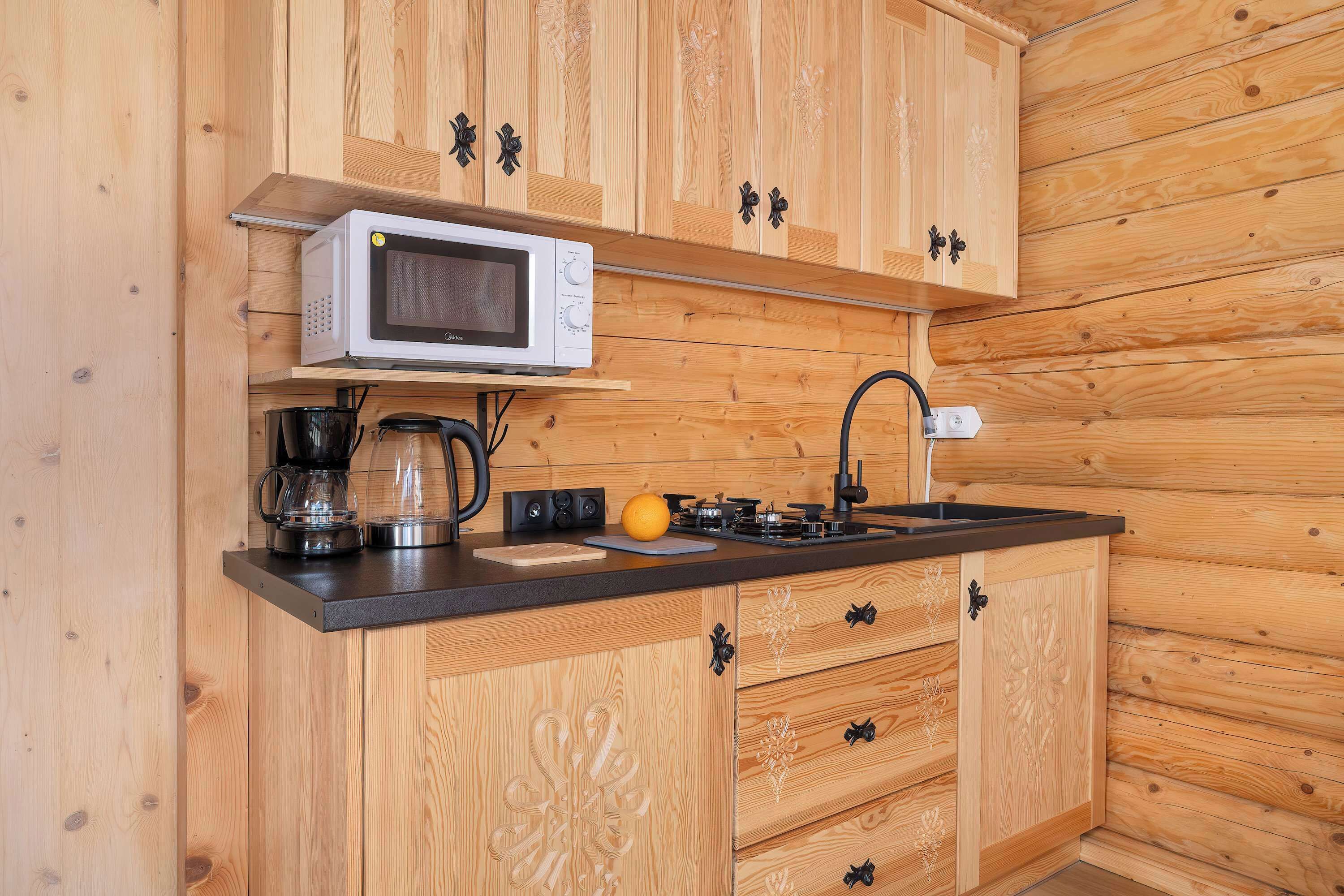 A wooden kitchen with a microwave, coffee maker, and orange on the counter.