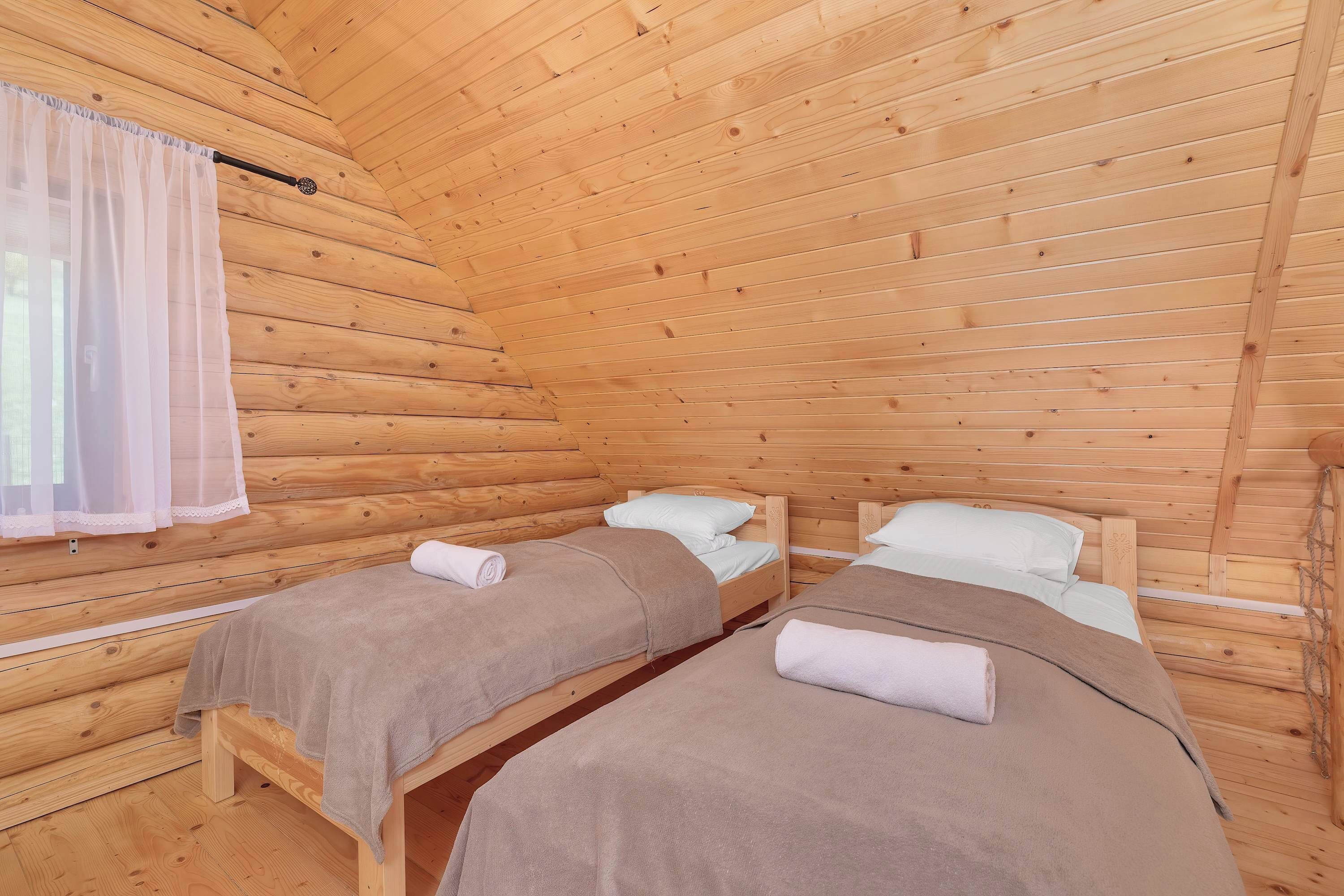 Une pièce de cabane en bois avec deux lits, une fenêtre avec un rideau léger et un plafond en bois.