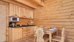 A wooden cabin interior with a kitchen area featuring wooden cabinets, a microwave, and a dining table with chairs. - A Charming House with a Garden | Mountain View (Mutne)