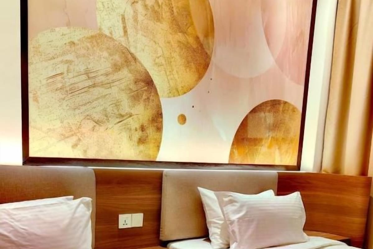 A hotel room with two beds, a large abstract painting above the beds, and a logo on the bedspread.