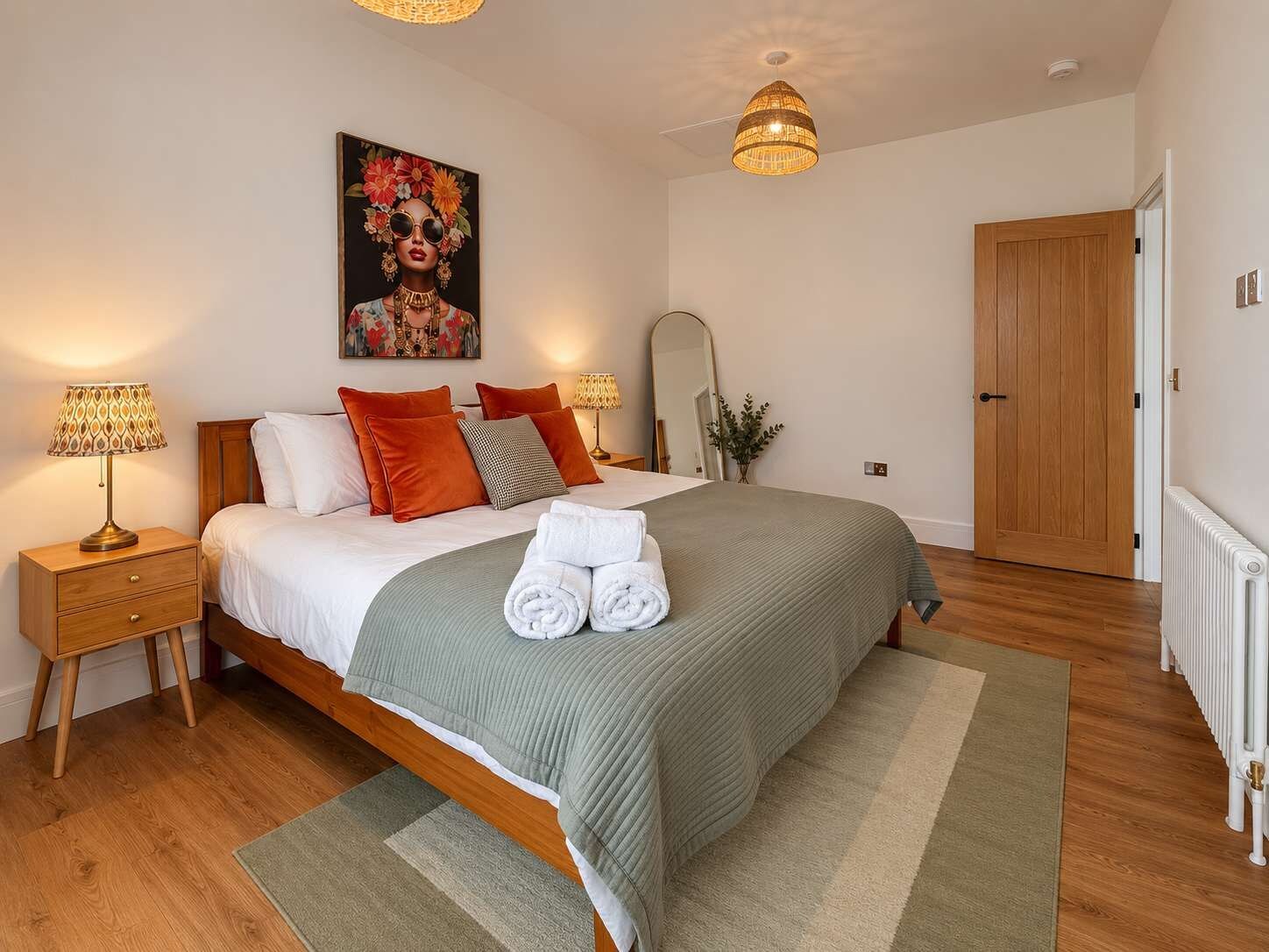 Quarto com cama, mesas de cabeceira, espelho e porta.