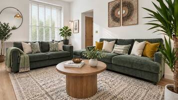 Ein Wohnzimmer mit zwei grünen Sofas, einem Holztisch und einem gemusterten Teppich.