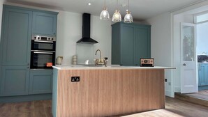 Une cuisine moderne dotée d’un îlot central, d’un four encastré et de luminaires suspendus.