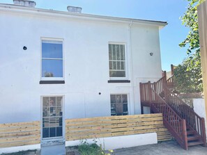 A white building with three windows, a wooden bench, and a wooden staircase. - The Headmaster’s Hideaway •Spacious 3BR with Patio (Cornwall)