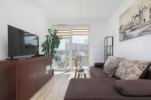 En moderne stue med et fladskærms-tv, en sofa, et sofabord og et stort vindue med persienner.