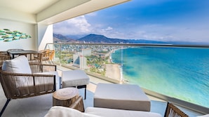 Un balcone con mobili in vimini, ringhiera in vetro e vista sull'oceano e sulla città.