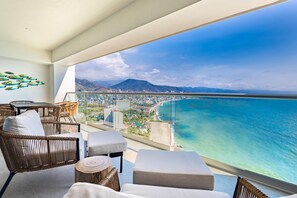 Ein Balkon mit Korbmöbeln, einer Glasumlaufung und Blick auf das Meer und die Stadt.