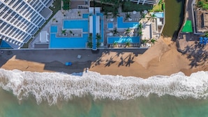 Una vista aerea di un resort con diverse piscine, una spiaggia e un grande edificio con facciata in vetro.