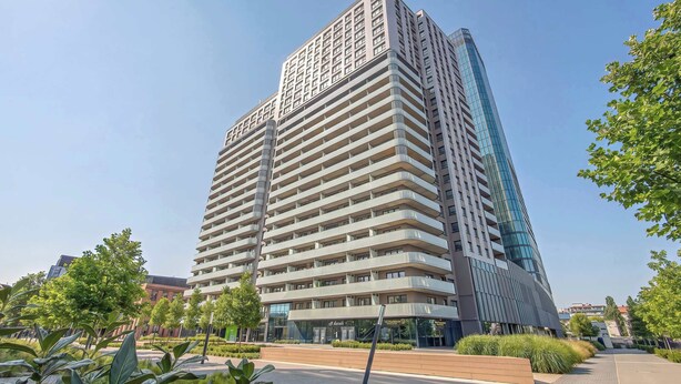 A multi-story building with a modern architectural design, featuring a prominent glass facade and a series of balconies. - Elegant Apartment with a View of the Oder River | Workspace | Parking | Balcony (Wrocław)