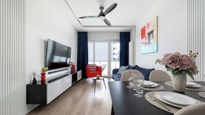 A modern living room with a flat-screen TV, a dining table set with plates and glasses, a red chair, and a ceiling fan. - Elegant Apartment with a View of the Oder River | Workspace | Parking | Balcony (Wrocław)