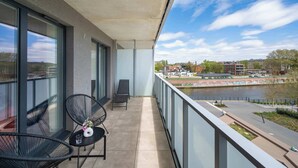 A balcony with two chairs, a small table with a vase and glass, and a view of a river and buildings. - Elegant Apartment with a View of the Oder River | Workspace | Parking | Balcony (Wrocław)