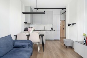 Et moderne køkken med hvide skabe, et spiseområde med sofa og stole, samt et lille sofabord med en vase.