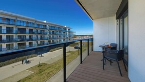 Un balcon donnant sur un immeuble moderne, une table avec des chaises et un ciel dégagé.