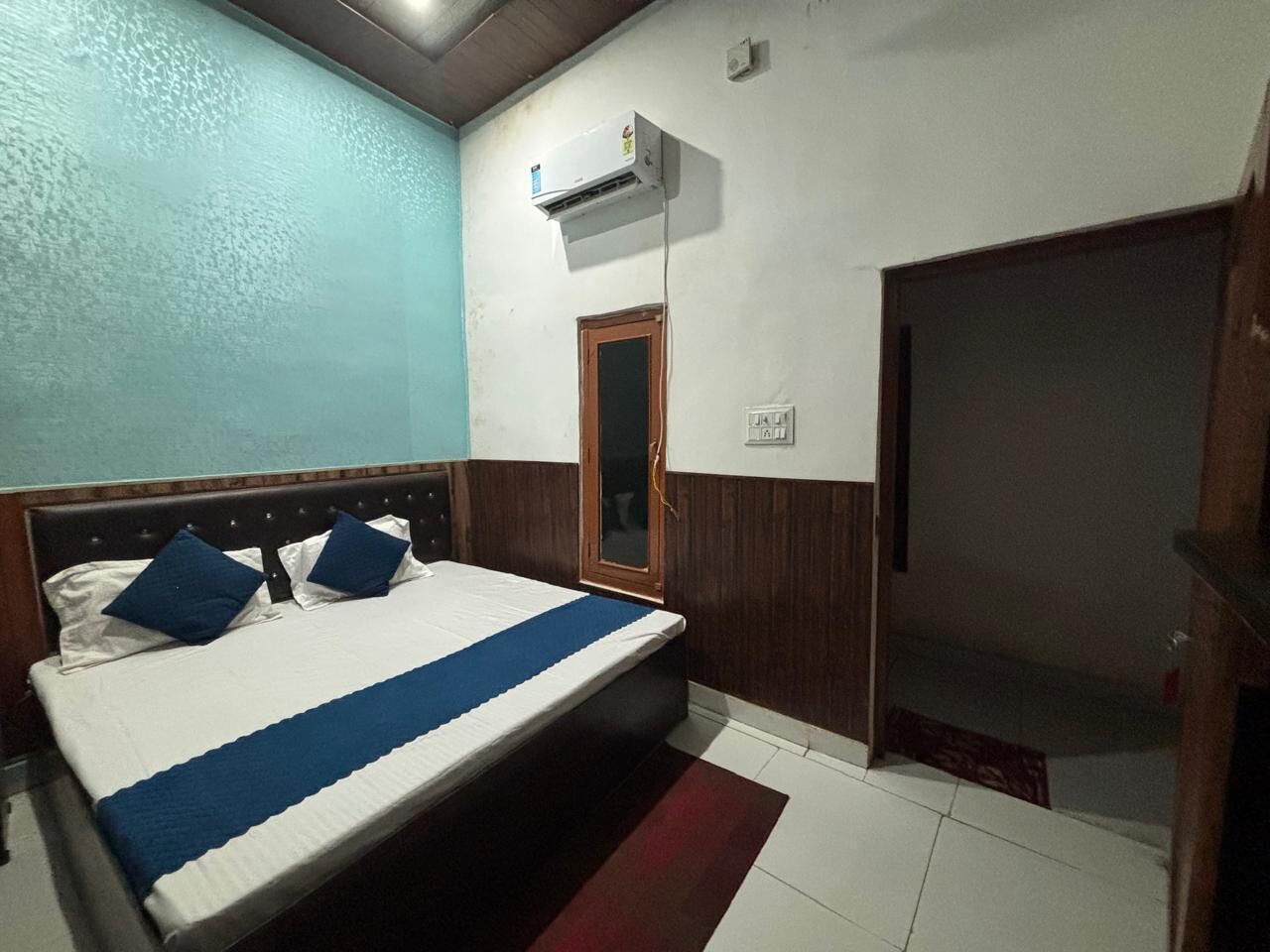 A bedroom with a bed, a wooden door, an air conditioning unit, and a small window.