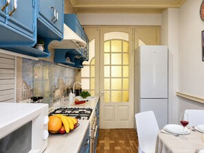 Una cocina compacta con armarios azules, una estufa blanca y un comedor con una mesa dispuesta para dos personas.
