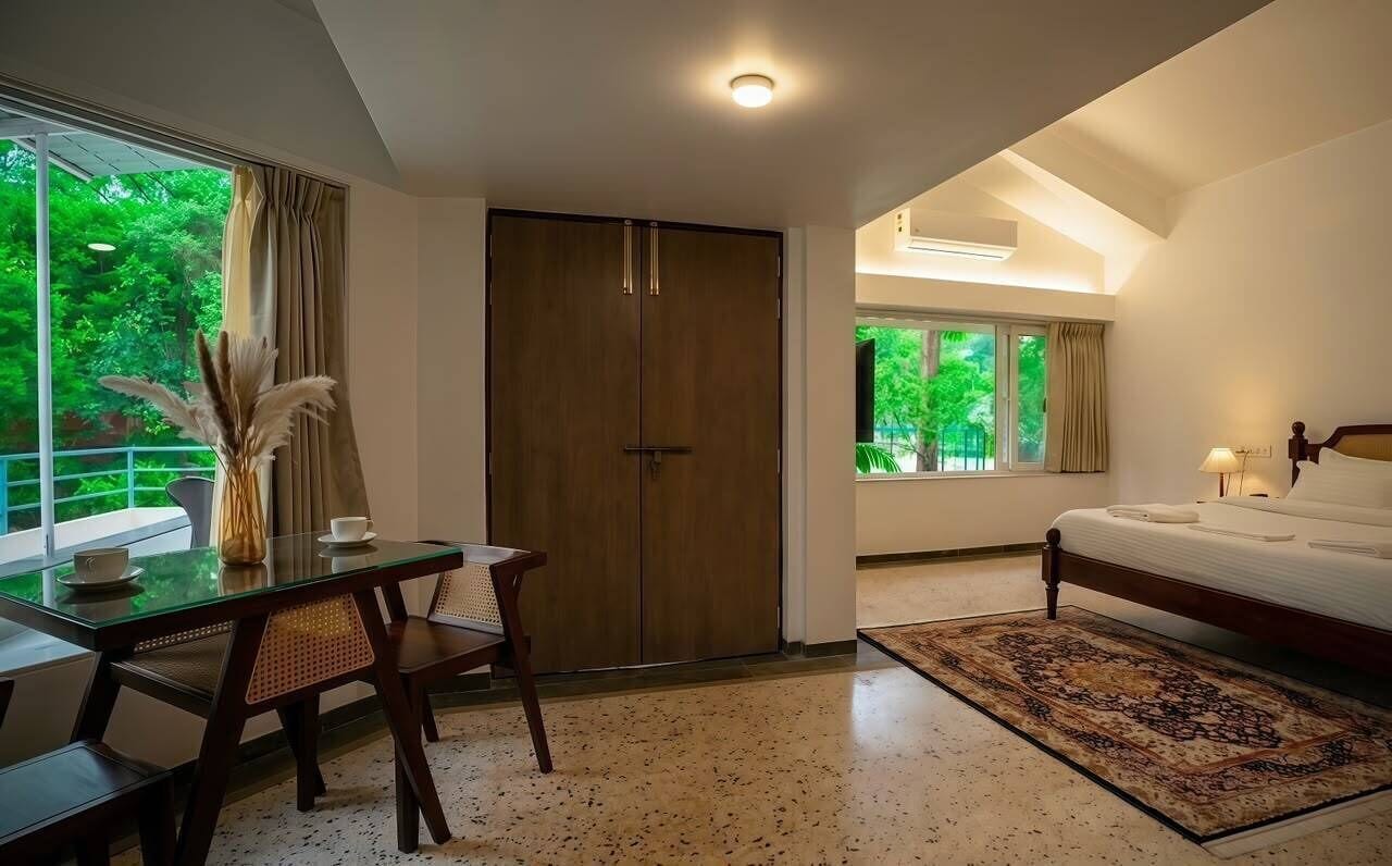 Habitación de hotel con cama, escritorio y una silla. Se ve un paisaje verde por la ventana.