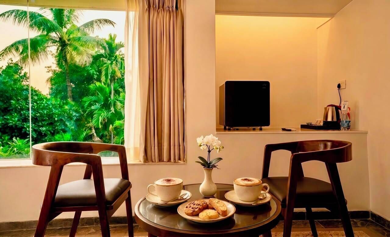 A room with a dining table, two chairs, a TV, a window with curtains, and a view of greenery outside.