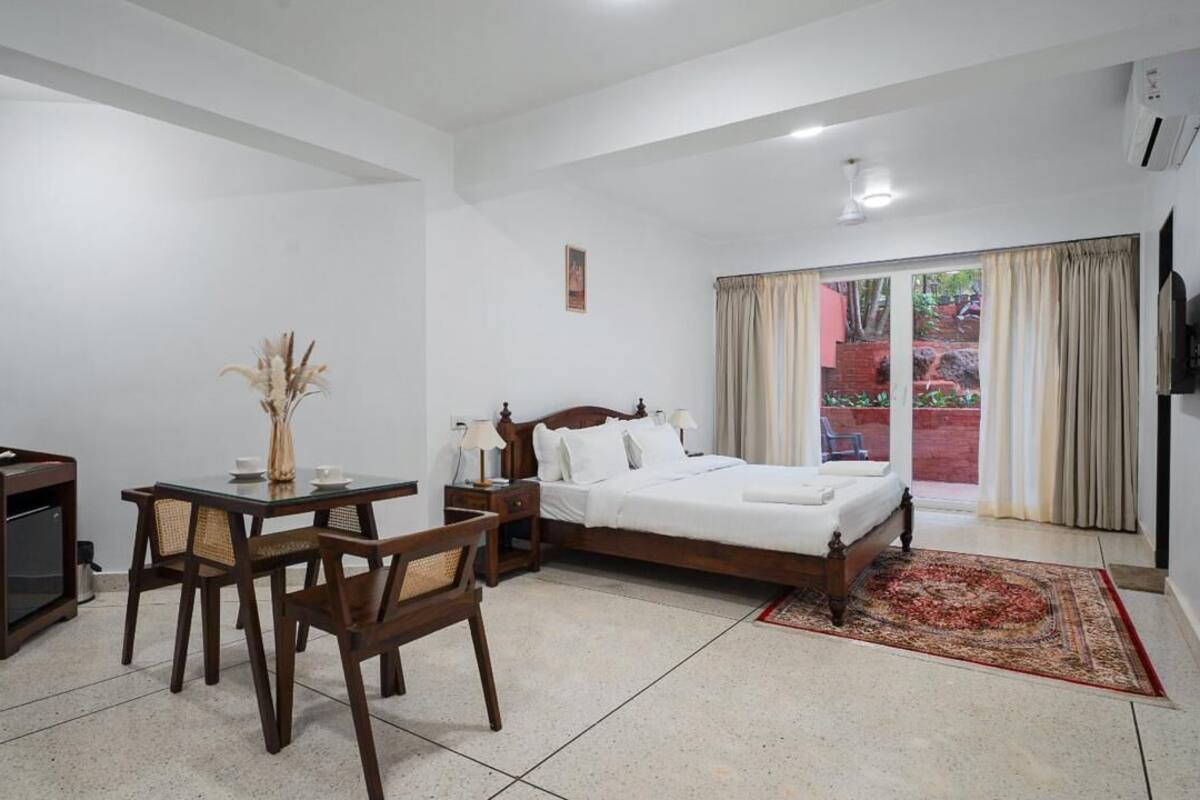 A hotel room with a bed, a desk with a chair, a television, and a window with curtains.