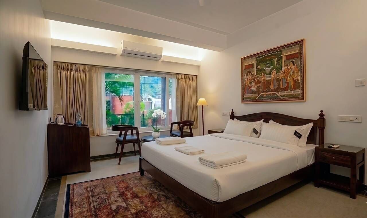 A hotel room with a large bed, a desk, a chair, a small table, and a painting on the wall.
