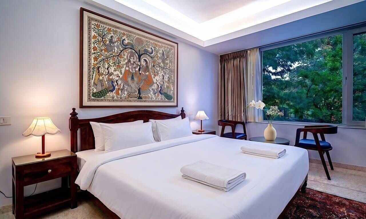 Ein Hotelzimmer mit einem großen Bett, zwei Nachttischen inklusive Lampen, einem Fenster mit Vorhängen und einem großen gerahmten Kunstwerk über dem Bett.