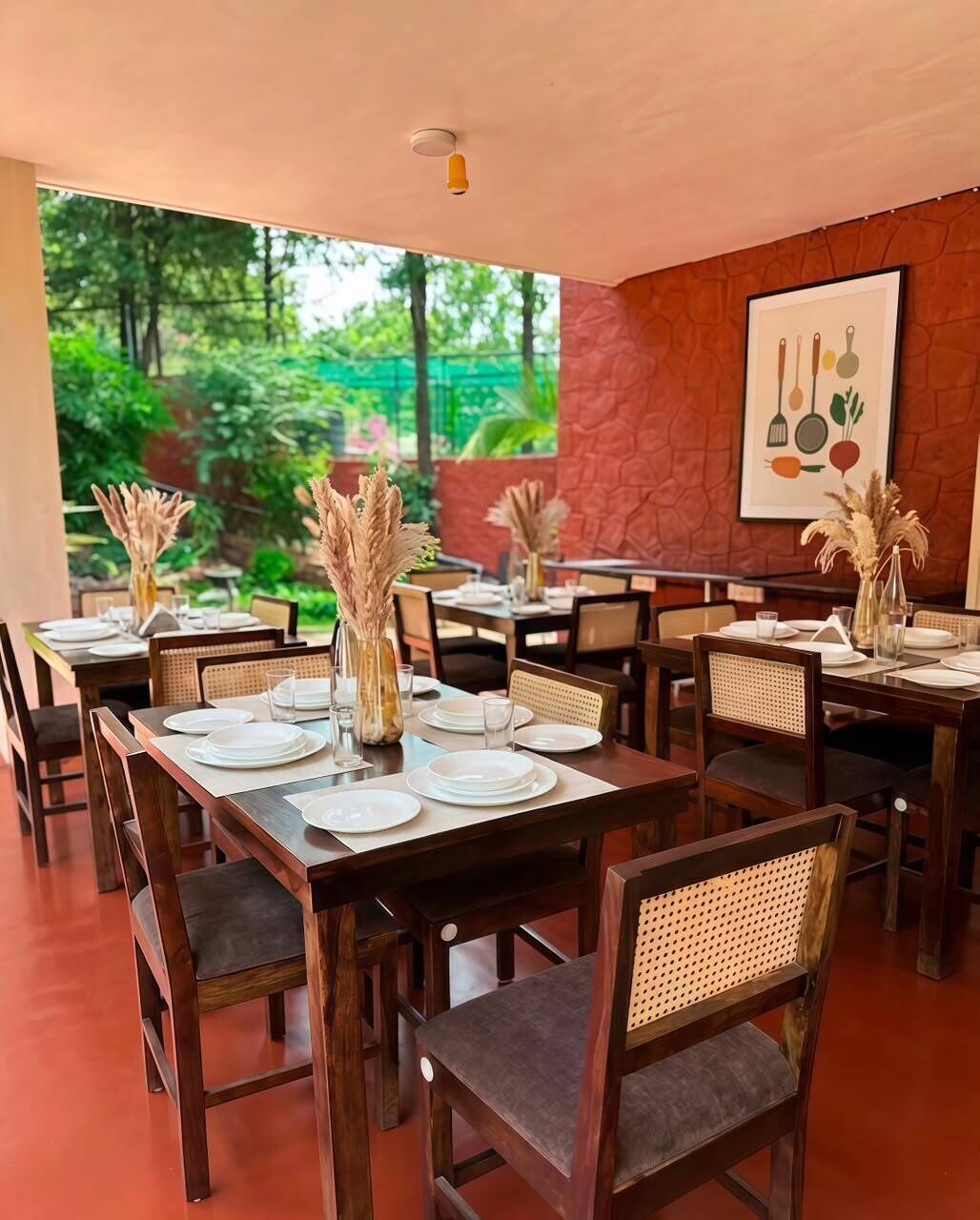 A restaurant with multiple tables set for dining, featuring a natural stone wall and a view of greenery.