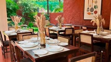 A restaurant with multiple tables set for dining, featuring a natural stone wall and a view of greenery.