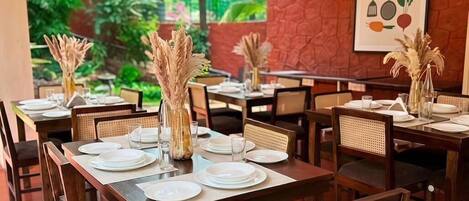 Un restaurant doté de nombreuses tables, avec un mur en pierre naturelle et une vue sur la verdure.