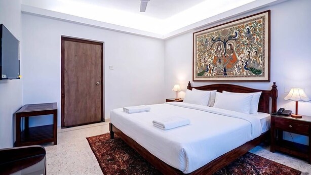 A hotel room with a bed, bedside lamps, a wooden door, a ceiling fan, and a large decorative painting on the wall.