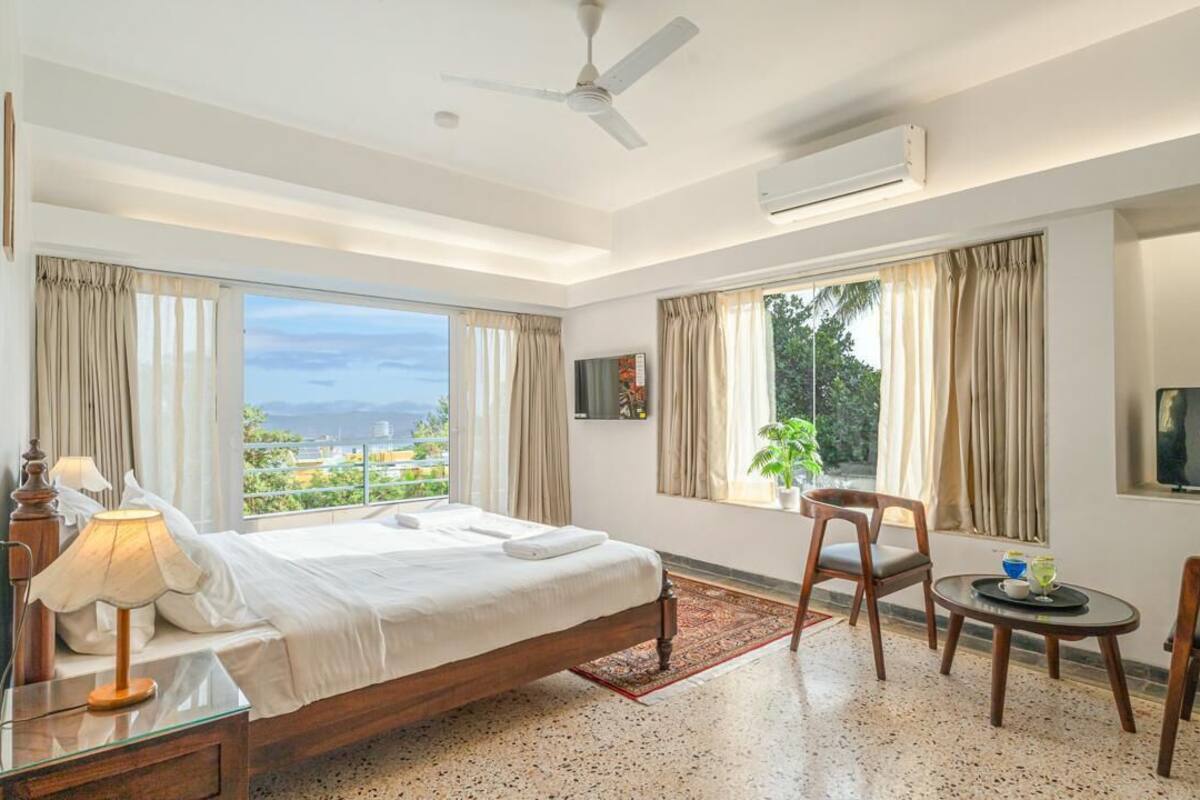 A hotel room with a bed, a desk, a chair, a TV, and a window with a view.